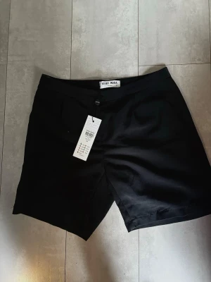Svarta shorts från Vero Moda - Stilrena svarta shorts från Vero Moda med klassisk passform och knapp framtill. Perfekta till sommaren och enkla att matcha med olika toppar. Gjorda i ett mjukt material som känns bekvämt hela dagen. Nya med lappar kvar . 