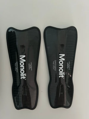 Monolit benskydd i kolfiber - Säljer ett par svarta benskydd från Monolit i kolfiber med slimmad design. De är lätta och har en blank finish. Kommer med en praktisk svart förvaringsväska med dragkedja. Perfekta för dig som vill ha skydd med låg vikt och hög komfort.
