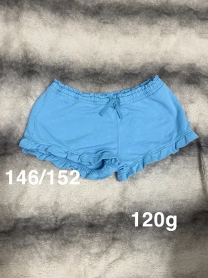Blå volangshorts med snörning - Snygga ljusblå shorts med volangkant och snörning i midjan. Perfekta för sommaren. Passar dig som gillar en söt och avslappnad stil.🌸 Fint använt skick. Storlek 146/152