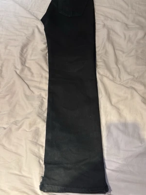 Levis Byxor (passar med häng) - Säljer ett par svarta jeans med rak passform och rå, fransad kant nedtill. Klassisk femficksmodell med knappgylf och nitar i kopparfärg. Perfekta för en avslappnad och trendig look.