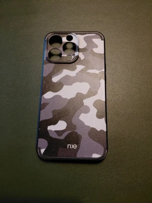 Nästan Nytt Camo mobilskal NXE iPhone 13 Pro - Nästan Nytt Snyggt mobilskal från NXE till iPhone 13 Pro med grått och svart camouflagemönster. Skalet är gjort i hårdplast och har exakta utskärningar för kameror och knappar. Perfekt för dig som vill ha ett unikt och tåligt skydd till mobilen.