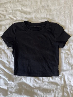 Svart ribbad crop t-shirt - Säljer en svart ribbad crop t-shirt från SHEIN. T-shirten har korta ärmar, rund halsringning och är tillverkad i ett mjukt, stretchigt material som sitter snyggt på kroppen. Perfekt till jeans eller kjol för en enkel och clean look.