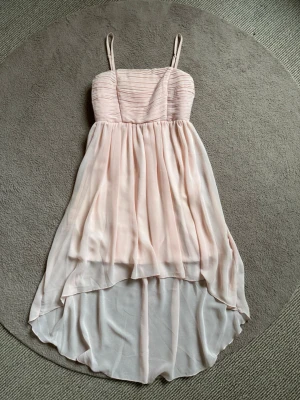 Ljusrosa klänning med mesh - Säljer en så vacker ljusrosa klänning som är längre bak och kortare fram, som visar benen fint💕Den har underkjol och tunna justerbara axelband. Överdelen har veckade detaljer och kjolen faller i flera lager med mesh material! Klänningen har dragkedja i ryggen och är tillverkad i ett tunt, flygigt material som ger en romantisk känsla😻Perfekt till sommaren, skolavslutning, events, firanden och speciella tillfällen🌸Komplimanger garanteras med denna klänning!! Barnstorlek 158, kan passa tonårsbarn❤️