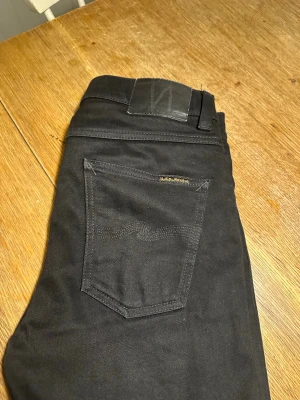 Svarta jeans från Nudie Jeans - Säljer ett par svarta jeans från Nudie Jeans med klassisk femficksmodell och diskret logga på bakfickan. Bara andvänd några gånger innan det blev för små för mig.