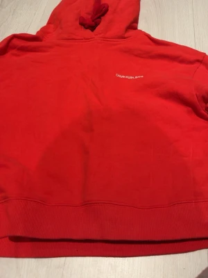 Röd magtröja från Calvin Klein - Snygg Calvin Klein jeanshoodie. Kortare i typen, magtröja. Med luva och coola detaljer på armar och rygg. 