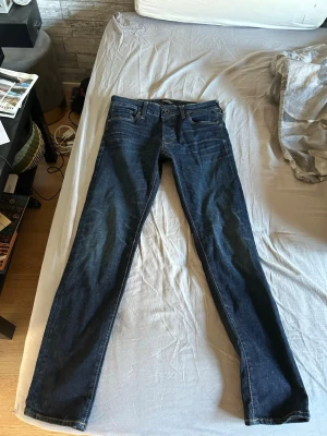Mörkblå slim fit jeans - Snygga mörkblå slim fit jeans med klassisk femficksdesign och raka ben. Jeansen har en läderpatch bak i midjan och subtila slitningar vid knäna. Perfekta för en stilren och avslappnad look.