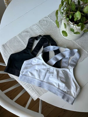 Toppar från Frank Dandy - Två toppar från Frank Dandy, en svart och en vit. Båda har breda axelband med logotyp och resår under bysten. Mjukt och stretchigt material  med brottarrygg.