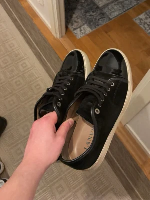Svarta Lanvin sneakers  - Snygga svarta sneakers från Lanvin med klassisk låg profil. Skorna har en kombination av mocka och glansigt lackläder på tån, samt vita sulor och metallfärgade öljetter. Perfekta för dig som gillar stilrena och exklusiva sneakers. Skorna är använda 3 gånger och i storlek UK 9, alltså storlek EU 43/44. OBS: 💥Lanvin Box ingår, lanvin dustbag till varje sko, helt nya original snören till skorna och sist men inte minst kvitto💥
