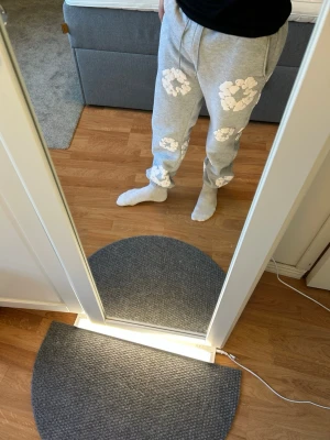 Denim tears  - Säljer ett par grå mjukisbyxor med vita blommönster. Byxorna har resår i midjan och vid bensluten samt sidofickor. Perfekta för en avslappnad stil och riktigt sköna att ha på sig. Materialet känns mjukt och bekvämt.