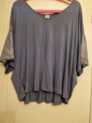 Blå oversized topp med spetsdetaljer - Säljer en blå oversized topp med v-ringning och breda, korta ärmar. Ärmarna har snygga spetsdetaljer som ger en extra touch. Perfekt för dig som gillar en avslappnad och trendig stil.