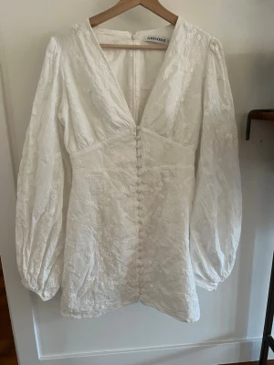 Klänning - Använd 1 gång. Supersöt vit klänning från Adoore med broderade blommor, v-ringning och långa puffärmar. Klänningen har knappar framtill och markerad midja som ger en snygg siluett. Perfekt för sommarens alla tillfällen! KOM MED PRISFÖRSLAG 