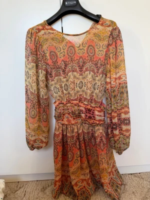 Trendig mönstrad klänning - Klänningen har lång ärm, markerad midja och cut-out detalj i sidan. Tillverkad i ett lätt, luftigt material som känns som polyester. 