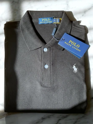 Svart pikétröja från Polo Ralph Lauren - Klassisk svart pikétröja från Polo Ralph Lauren med vit broderad logga på bröstet. Tröjan har krage, knäppning med två knappar och är tillverkad i bomull. Perfekt till en stilren och avslappnad look.