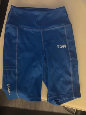 Blå träningstights shorts ICANIWILL - Snygga blå träningstights shorts från ICANIWILL med hög midja och praktiska sidofickor. Tillverkade i stretchigt syntetmaterial som passar perfekt för träning. Logga på benet och fickan ger en sportig look.