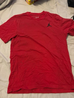 Röd Jordan t-shirt med logga - Snygg röd t-shirt från Jordan med klassisk Jumpman-logga i svart på bröstet. Tillverkad i mjuk bomull och har rund halsringning samt korta ärmar. Perfekt för en sportig och avslappnad stil.