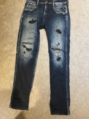 Mörkblå slitna jeans med hål - Säljer ett par mörkblå jeans med kraftiga slitningar och hål på både fram- och baksida. Jeansen har skinny fit, fem fickor och cool tvätt med ljusare partier. Perfekta för dig som gillar en edgy streetstil.
