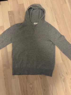 Cashmere Hoodie - Mjuk och stilren grå hoodie från Sayless i cashmere. Klassisk modell med huva och dragsko, ribbade muddar vid ärmslut och nederkant. Perfekt för dig som gillar en enkel men lyxig look. Slitage vid halsen