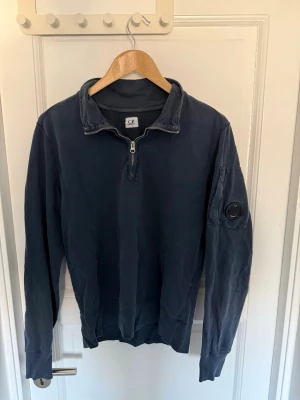 Mörkblå half-zip tröja från C.P. Company - Mörkblå, robust, långärmad tröja från C.P. Company med half-zip dragkedja och hög krage. Vid fler frågor eller intresse av fler bilder är det bara att höra av sig🤠