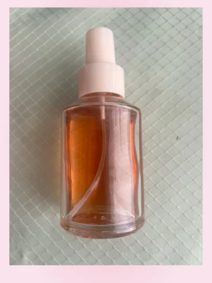 Stark caramel parfym - Säljer en stilren parfymflaska i genomskinligt glas med vitt spraymunstycke. Flaskan innehåller en vätska i orange ton och har en enkel, rund form. Perfekt för dig som gillar minimalistisk design och vill ha en snygg detalj på sminkbordet.🩷