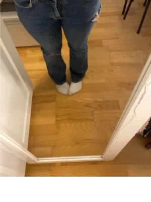 Blå slitna jeans - Säljer ett par blå jeans, utsvängda bootcot och slitningar vid knäna. Jeansen har klassisk femficksdesign och normal midja. Perfekta för en avslappnad och trendig look.