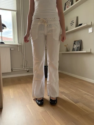 Vita linnebyxor med snörning - Säljer ett par vita linnebyxor med raka ben och snörning i midjan. Byxorna har stora fickor både fram och bak och är tillverkade i ett lätt och luftigt linnematerial. Perfekta för en avslappnad och stilren look.