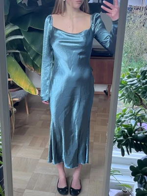 Ljusblå långklänning i satin - Säljer en elegant ljusblå långklänning i glansigt satinmaterial. Klänningen har långa ärmar och figurnära passform. Perfekt till baler, sittningar och andra tillställningar!