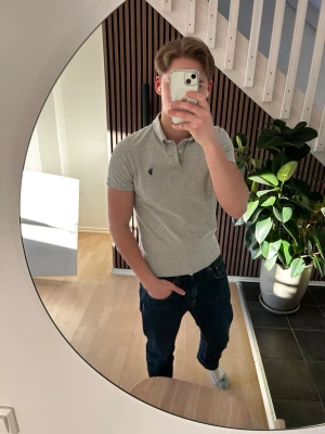 Ljusgrå pikétröja från polo - Säljer en stilren ljusgrå pikétröja från us polo assn med klassisk krage och knappar framtill. Tröjan har korta ärmar och den ikoniska loggan broderad på bröstet. Perfekt till jeans eller shorts för en clean look.