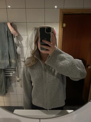 Grå stickad ziptröja från BikBok - Mysig grå stickad tröja från BikBok med dragkedja framtill och hög krage. Tröjan har en ribbstickad struktur och långa ärmar💞