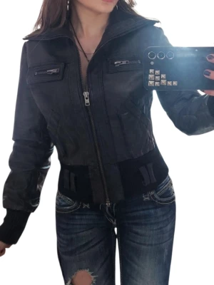 Svart skinnjacka  - Snygg svart skinnjacka med ribbade muddar och bred midjeresår. Jackan har två bröstfickor med dragkedja, två sidofickor och coola detaljer på midjan. 