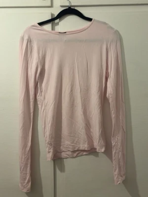 Ljusrosa långärmad topp Gina Tricot - En enkel och stilren ljusrosa långärmad topp från Gina Tricot. Toppen har rund halsringning och är gjord i ett mjukt material som känns skönt mot huden. Perfekt att matcha med jeans eller kjol för en clean look. Använd 1 gång