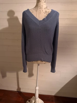 Blå stickad V-ringad tröja - Säljer en stilren blå stickad tröja med V-ringning och långa ärmar. Tröjan har en grovstickad struktur och breda ribbade muddar vid ärmslut och nederkant. Perfekt för dig som gillar en enkel men snygg look.