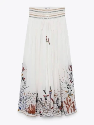 Vit långkjol med broderi och snörning - Säljer en supersnygg vit långkjol med färgglada broderade detaljer i nederkant och snörning i midjan. Kjolen har ett vågigt mönster upptill och fina broderier med korall  motiv. Perfekt för sommaren! 