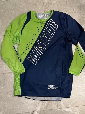 Motorcross tröja från Wicked Family sporttröja blå/grön - Snygg långärmad sporttröja från Wicked i blått och limegrönt med stora logotexter och prickdetaljer. Tillverkad i ett lätt och ventilerande funktionsmaterial, perfekt för intensiva aktiviteter. Tröjan har rund hals och en modern, sportig design. Det är endast använt ett fåtal gånger eftersom att jag lagt av med cross några veckor efter att vi köpt tröjan.  Nypris är 600kr