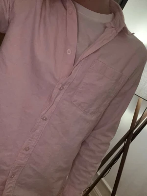 Ljusrosa skjorta m - Säljer en stilren ljusrosa skjorta med klassisk krage och bröstficka. Skjortan har knappar hela vägen och långa ärmar. Perfekt att matcha med jeans eller linnebyxor för en clean look. Perfekt till våren och sommaren
