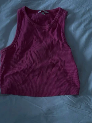 Rosa ribbad linnetopp från H&M - Säljer en rosa ribbad linnetopp från H&M i storlek M. Toppen är ärmlös och har en croppad passform som passar perfekt till både jeans och kjol. Materialet är mjukt och stretchigt för en bekväm känsla.
