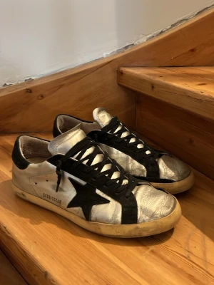 Silverfärgade Golden Goose sneakers - Snygga sneakers från Golden Goose i metallic silver med svarta detaljer. defekt bak på sulan, se bild 4. Använda men liv kvar skriv vid intresse!