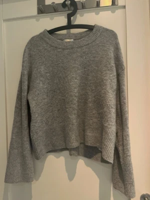 Grå croppad stickad tröja från Gina Tricot - Mysig grå stickad tröja med croppad passform och breda ribbade muddar vid ärmslut och nederkant. Tröjan har rund halsringning och är tillverkad i ett mjukt material som passar perfekt till kyligare dagar. Storlek 158/164, vilket är ungefär XS.