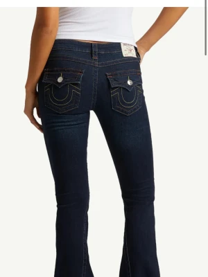 Mörkblå bootcut jeans True Religion - Snygga mörkblå bootcut jeans från True Religion med ikoniska bakfickor och kontrastsömmar. Jeansen har låg midja och silverfärgade knappar på fickorna. Perfekta för en trendig och avslappnad look. superbra skick❤️ De är uppsydda ca 5-10 cm