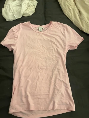 Ljusrosa t-shirt från New yorker  - En basic ljusrosa t-shirt från New yorker med rund halsringning och korta ärmar. Tillverkad i mjuk bomull som känns skön mot huden. Perfekt att matcha med jeans eller kjol för en enkel och clean look.