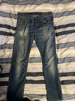 Feta Blå slitna jeans från G-Star RAW - Säljer ett par blå jeans från G-Star RAW med snyggt slitna detaljer och klassisk femficksmodell. Jeansen har raka ben och tydliga slitningar framtill och baktill för en cool, avslappnad look. Materialet är robust denim i bomull.