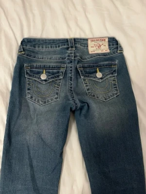 Blå bootcut jeans från True Religion - Snygga blå jeans från True Religion med klassiska kontrastsömmar och ikoniska bakfickor med lock och knapp. Har andra par i W26 oxå. Aldrig använda fel storlek postar så snabbt🥰