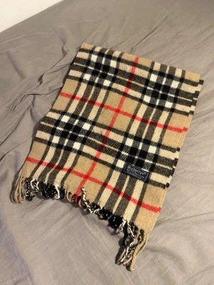 Burberry halsduk - Exklusiv och tidlös halsduk från ikoniska lyxmärket Burberry. Klassiska rutmönstret som aldrig går ur stil och passar perfekt till både vardag och mer uppklädda outfits. Väldigt mjuk och varm – ett riktigt premiumplagg.