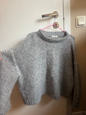 Grå stickad tröja - Mysig grå stickad tröja som jag köpte på vero Moda med vita dekorativa sömmar längs axlar och ärmar. Tröjan har en avslappnad passform, rund halsringning och ribbade muddar. Perfekt för kalla dagar och enkel att styla till olika outfits.