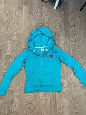 Turkos hoodie från PINK - Säljer en turkos hoodie från Victorias secret-PINK med dragkedja framtill och stor huva. Hoodien i bomullsmaterial, perfekt för chill dagar eller när du vill ha en avslappnad look.