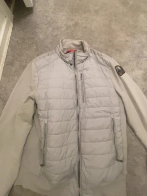 Ljusgrå fleecejacka Parajumpers L - Snygg ljusgrå fleecejacka från Parajumpers med quiltad front och dragkedja. Jackan har hög krage, två sidofickor med dragkedja och en bröstficka. Märkespatch på ärmen och sportig look. Perfekt för lager på lager under kyliga dagar.