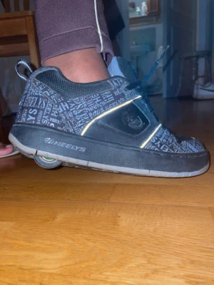 Rullskor, Heelys [Str.40] - Ett par Heelys - rullskor. Står 40.5, men de är storlek 40. Skorna har snörning, rund tå och inbyggda hjul i sulan så du kan rulla fram. Ovandelen är i syntet och skinn, och sulan är grå. Perfekt för dig som vill glida runt med stil!