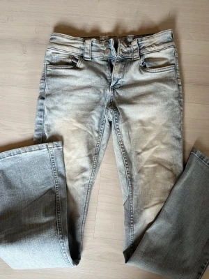 Ljusblå bootcut jeans med fickdetaljer Storlek 164!! - Säljer ett par ljusblå bootcut jeans med snygga fickdetaljer och knappar bak. Jeansen har klassisk femficksdesign, bälteshällor och är tillverkade i mjukt denimtyg. Perfekta för dig som gillar en avslappnad men trendig look. Storlek 164!