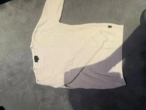 Beige stickad tröja från D.M.D - Snygg beige stickad tröja från D.M.D med rund halsringning och ribbade muddar. Tröjan har ett diskret rutmönster i stickningen och en klassisk, avslappnad passform. Perfekt för lager på lager och enkel att matcha med olika stilar.