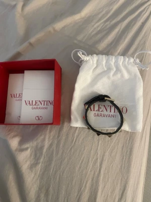 Svart armband Valentino Garavani - Snyggt svart armband från Valentino Garavani med coola nitar runt hela bandet. Armbandet har en stilren och edgy design, perfekt för att lyfta din outfit. Kommer med original ask och dustbag från Valentino. Pris kan diskuteras