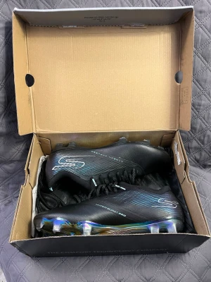 Svarta Skechers fotbollsskor - Skechers Razor , Snygga svarta fotbollsskor från Skechers med en stilren design och diskreta blå detaljer. Skorna har en syntetisk ovandel och en färgglad, mönstrad yttersula med dobbar för bra grepp på planen. Perfekta för dig som vill sticka ut på fotbollsplanen.